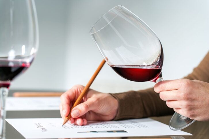 hand holding wine glass, other hand writing with pencil in hand