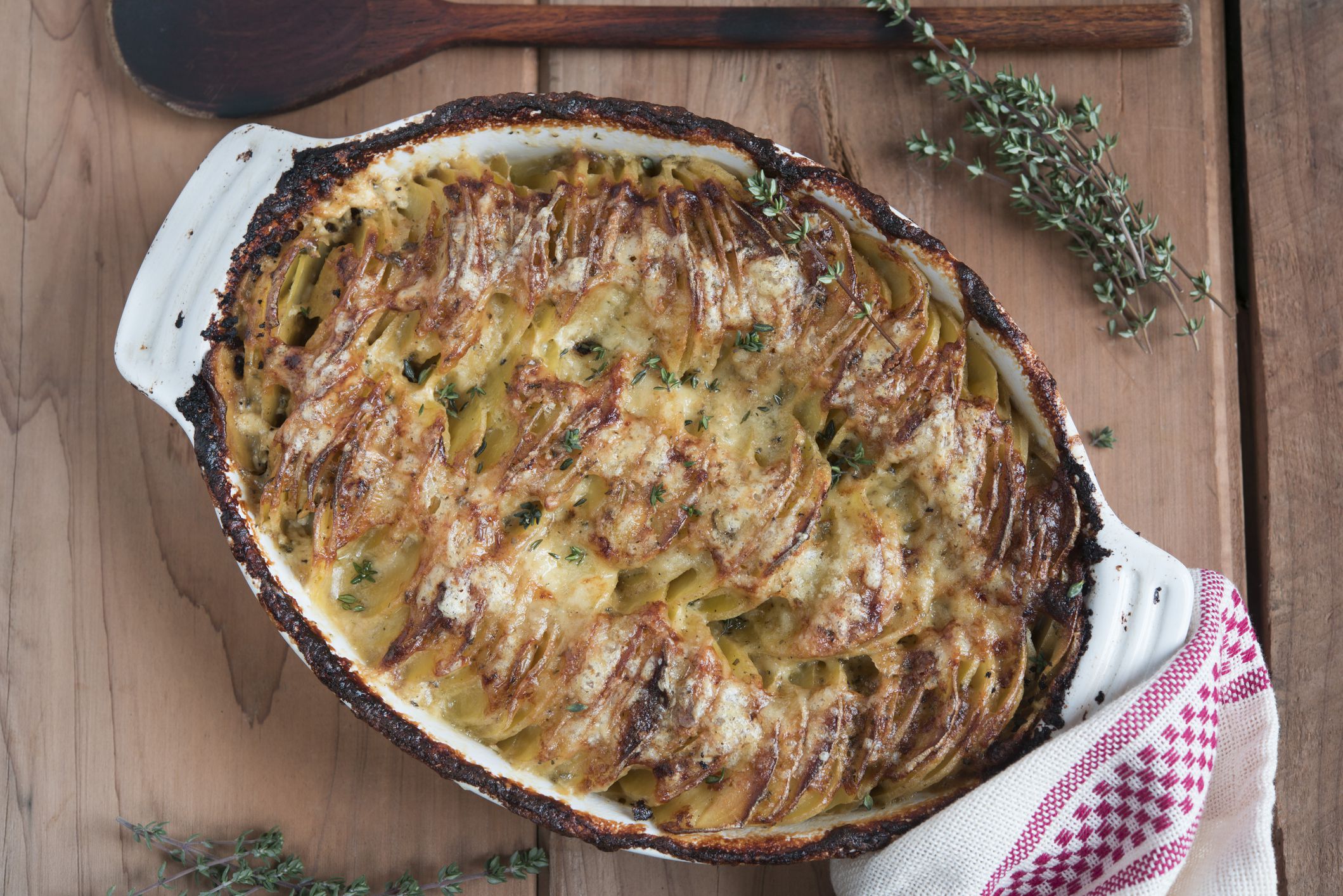 Au gratin or hasselback potatoes in a white dish on wood surface with thyme