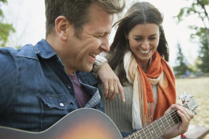 man playing guitar for wife in park