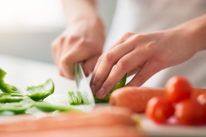 person cutting green pepper in kitchen with kitchen knife