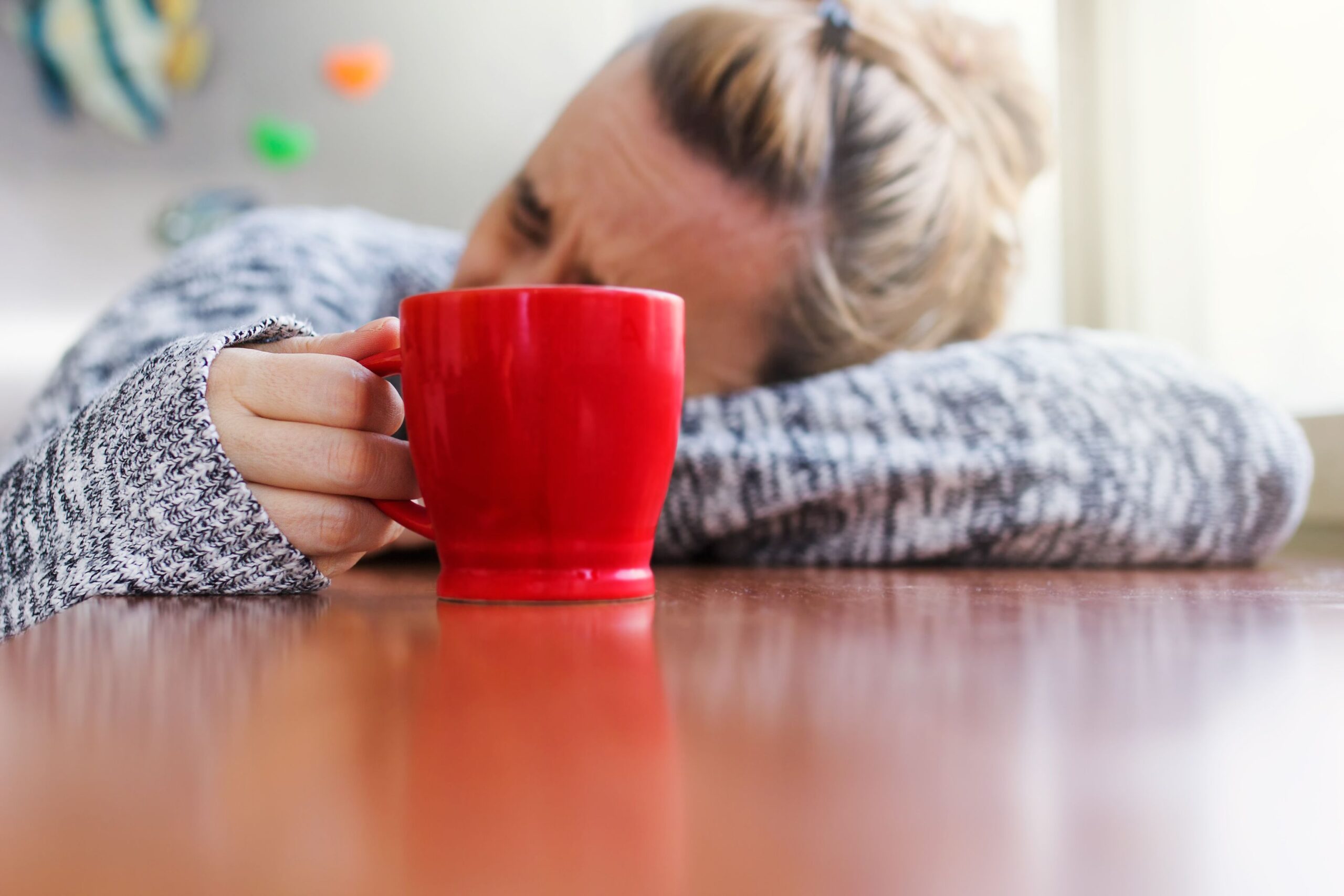 Depressed woman laying on a desk with a cup of coffee in hand