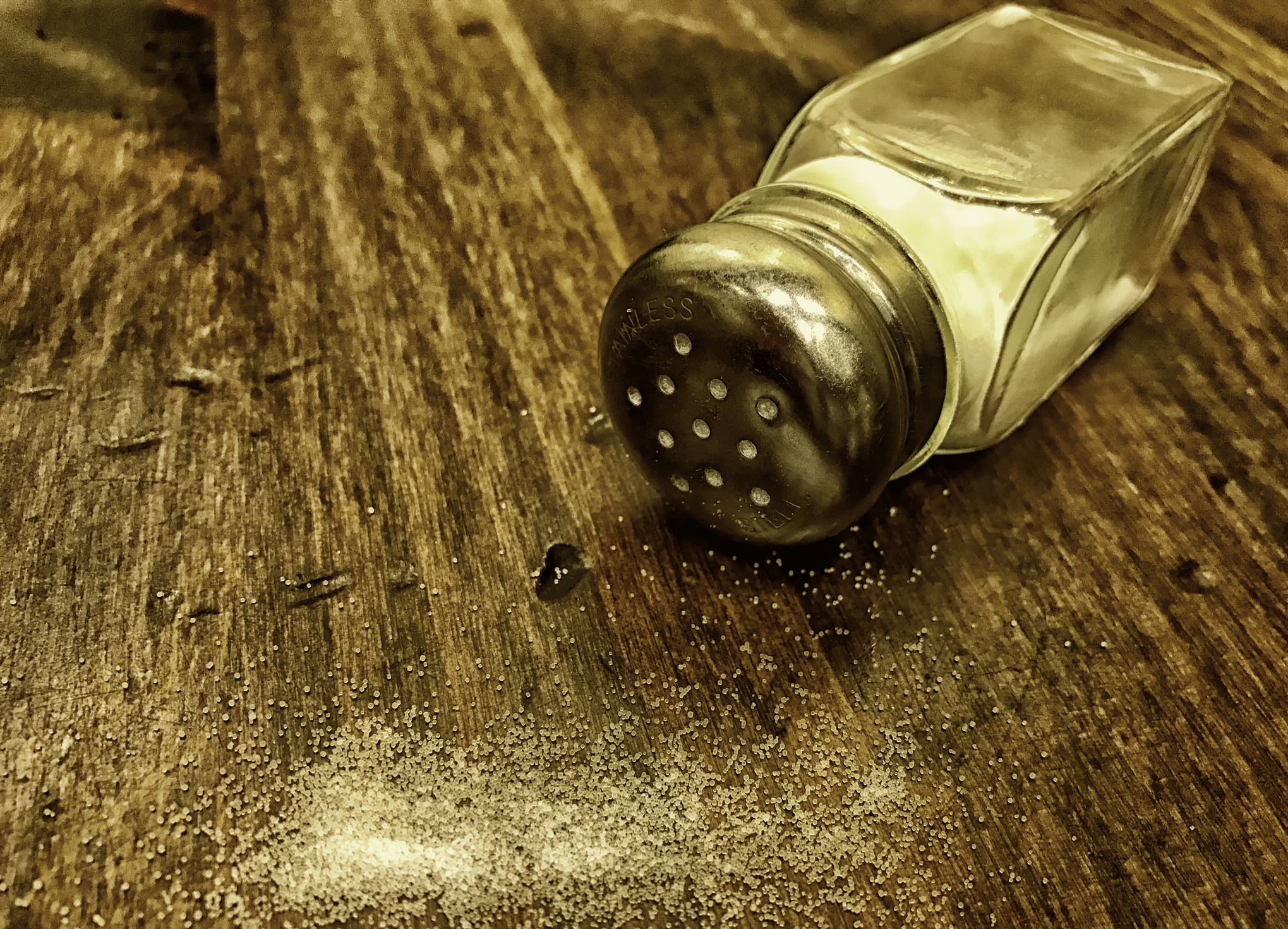 Salt shaker on its side with spilled salt. Close-up, color photo.