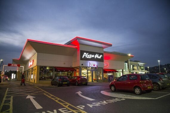 Swansea, UK: December 27, 2016: People walk past a night time drive through. Pizza Hut is an American restaurant chain and international franchise, known for its Italian-American cuisine menu including pizza and pasta.