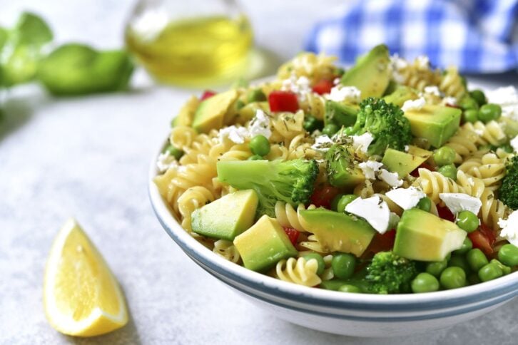 Pasta salad with green vegetables and feta in a vintage plate on a light concrete,stone or slate background.
