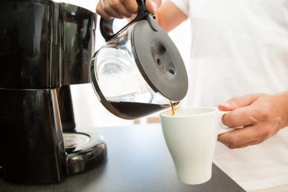 Man in the kitchen pouring a mug of hot filtered coffee from a glass pot. Having breakfast in the morning