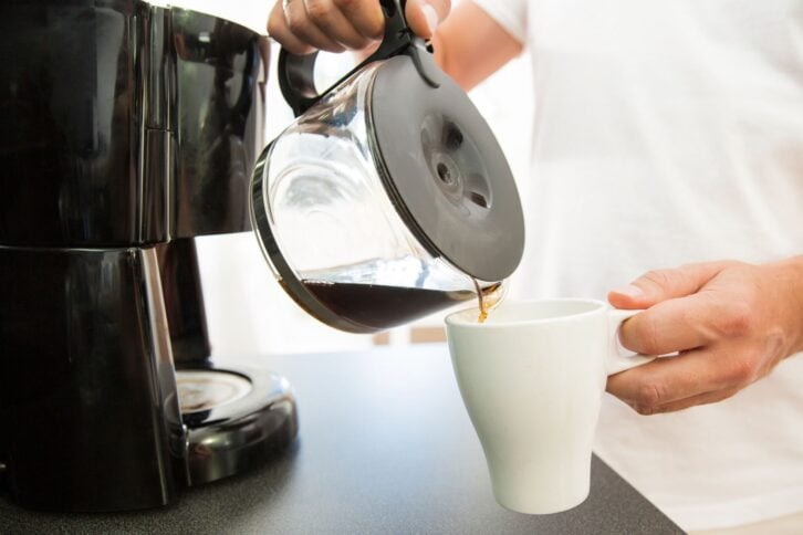 Man in the kitchen pouring a mug of hot filtered coffee from a glass pot. Having breakfast in the morning