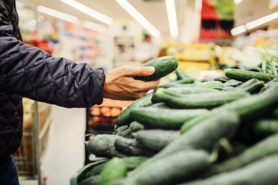 Young Man Groceries Shopping. Standing in front of produce stand and choosing cucumber