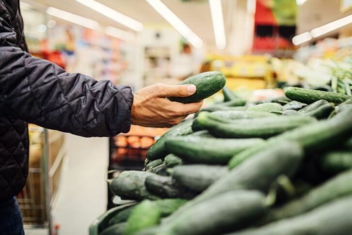 Young Man Groceries Shopping. Standing in front of produce stand and choosing cucumber