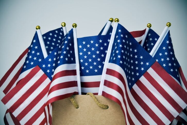 closeup of some flags of the United States in a brown paper shopping bag, with a vignette added