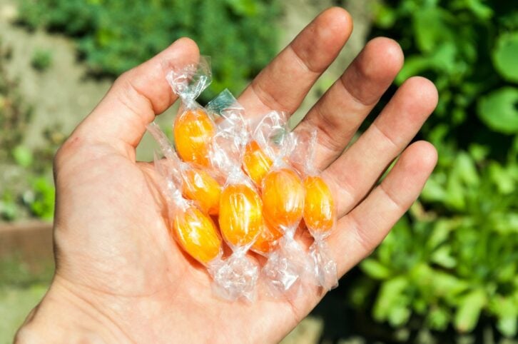 Male hand holding candy in cellophane. Outdoor.