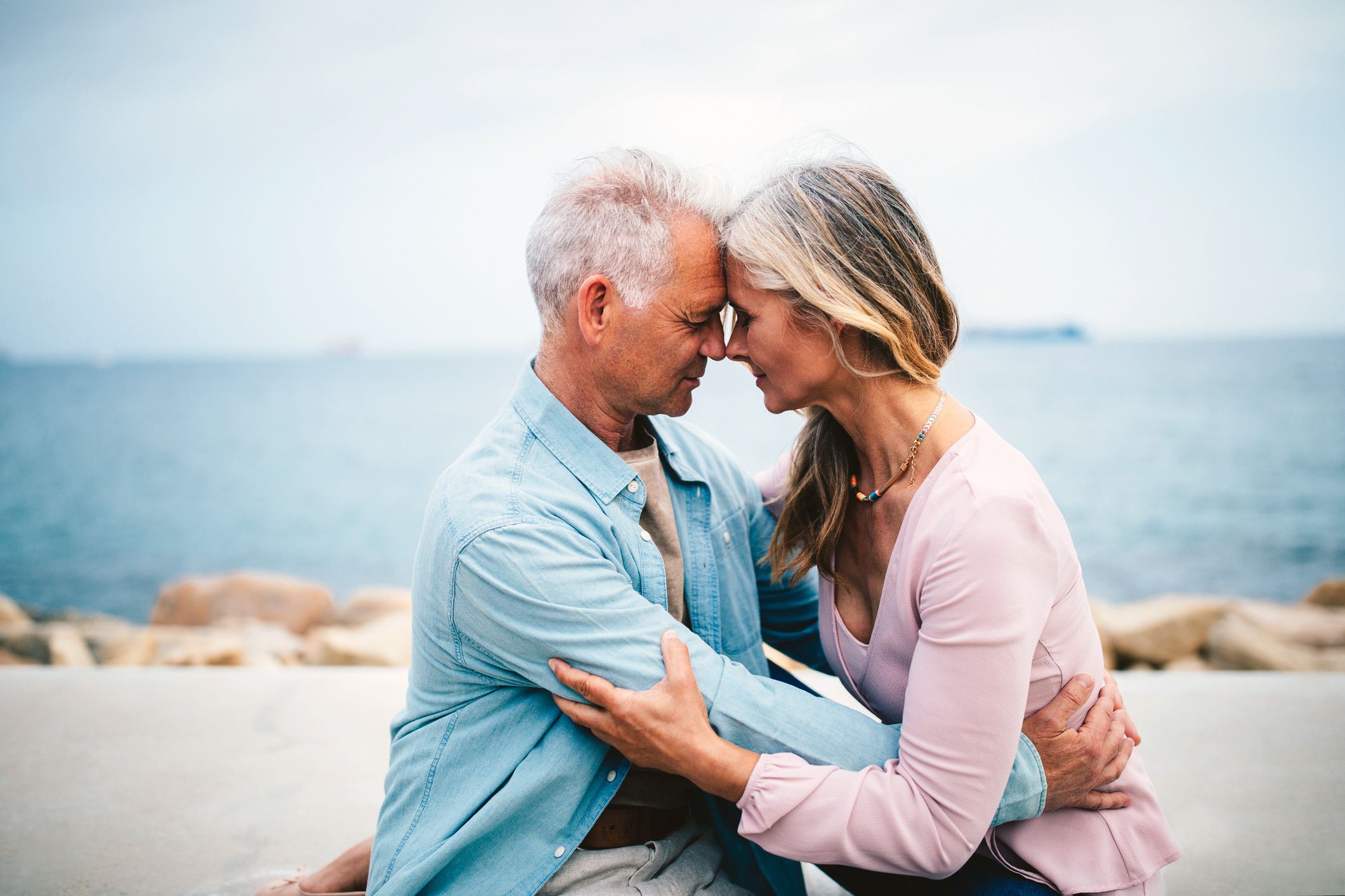 senior couple embracing with eyes closed with beach in background