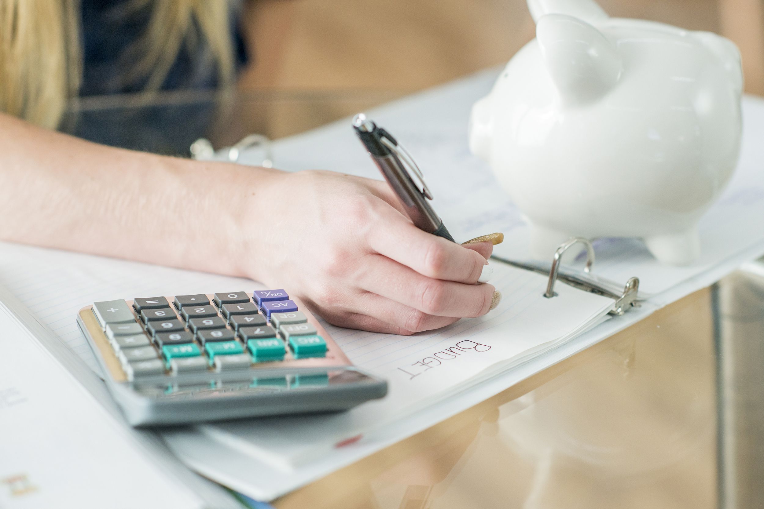woman doing budget in binder with piggy bank and calculator