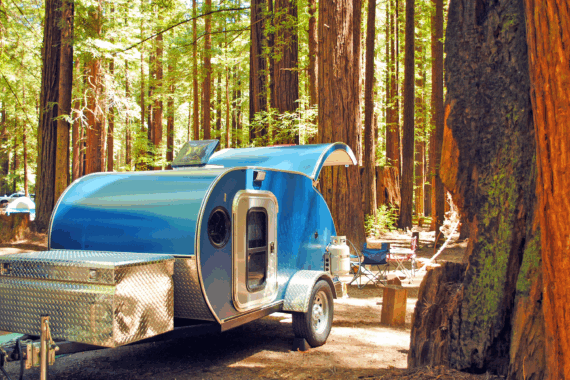 A blue teardrop camping trailer is setup at a campsite surrounded by redwood trees in Humboldt Redwoods State Park in California