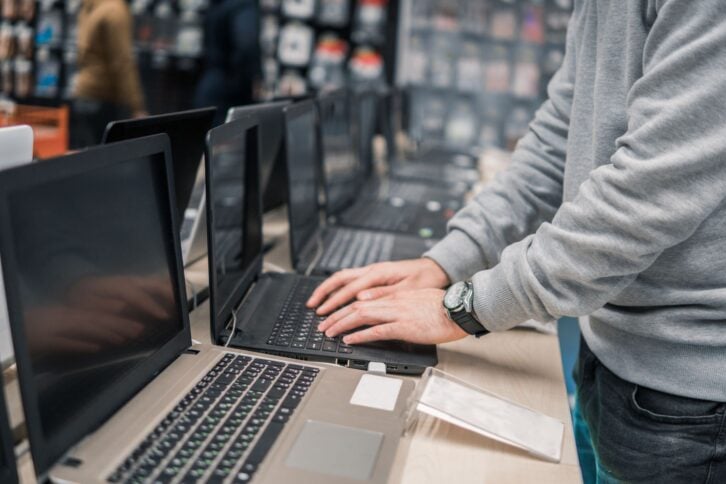 Smart modern male customer choosing laptop in the computer store. difficult decision. He is opening notebook for checking.