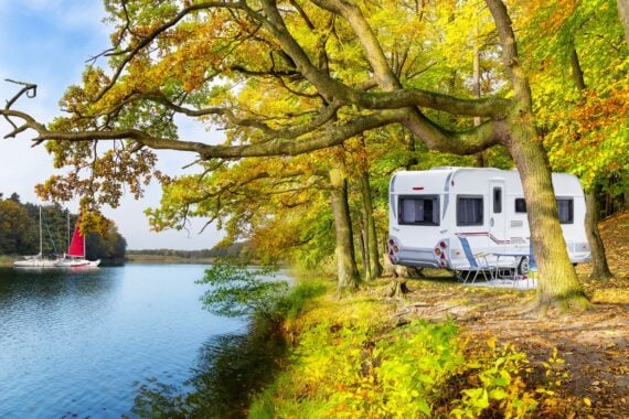 rv on shore of lake, sailboats in distance