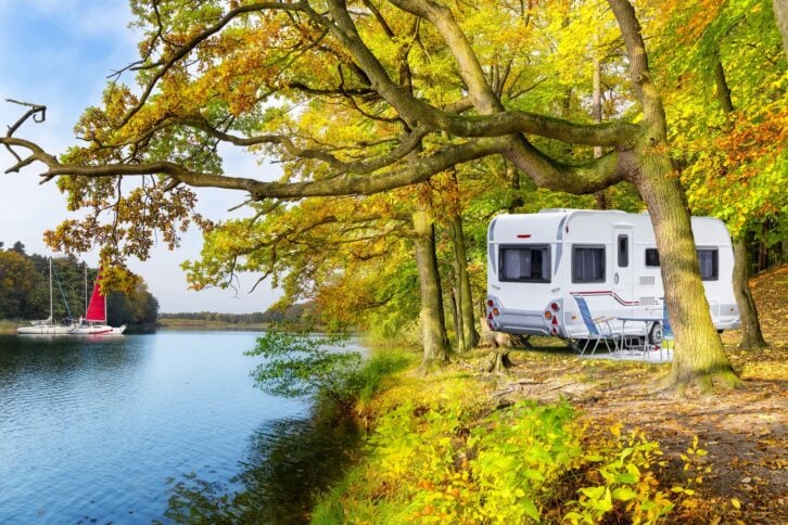 rv on shore of lake, sailboats in distance