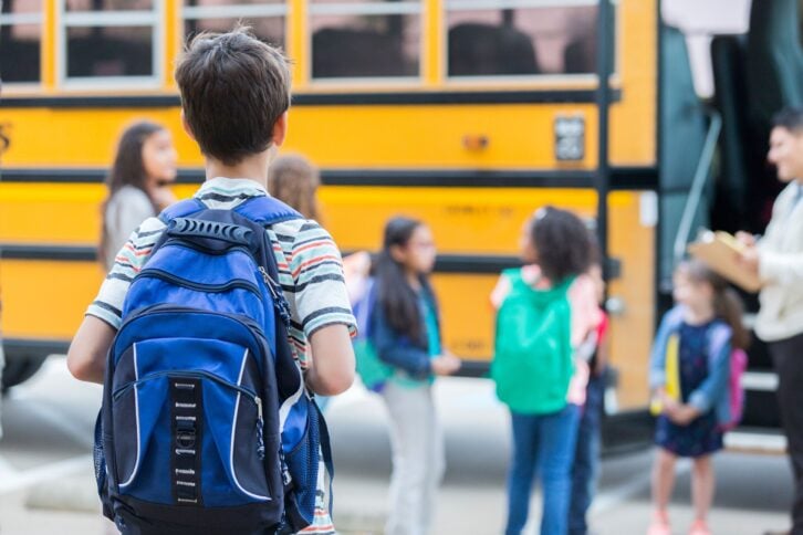 young boy waits to load school bus, wearing backpack