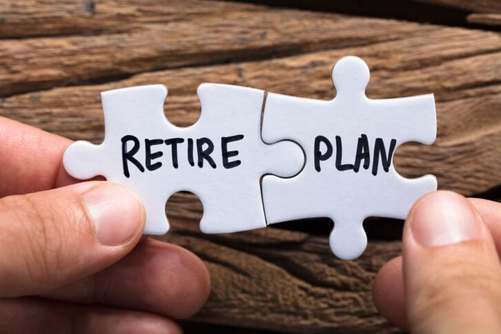 closeup of hands holding retire plan matching jigsaw pieces against wood