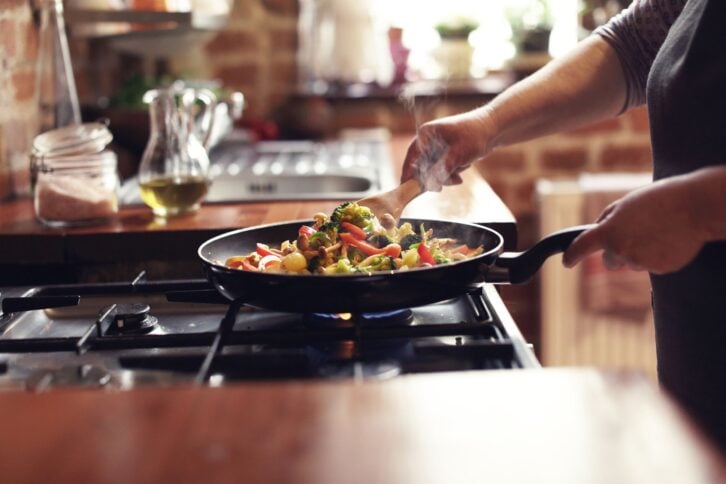 person cooking stir fry in pan on stove in the kitchen