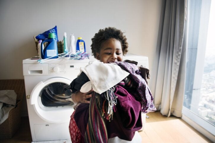young boy carrying laundry in front of washer and dryer