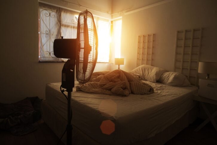electric fan in-front of an unmade bed