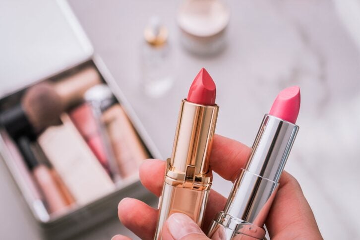 hands holding two lipsticks with makeup in background