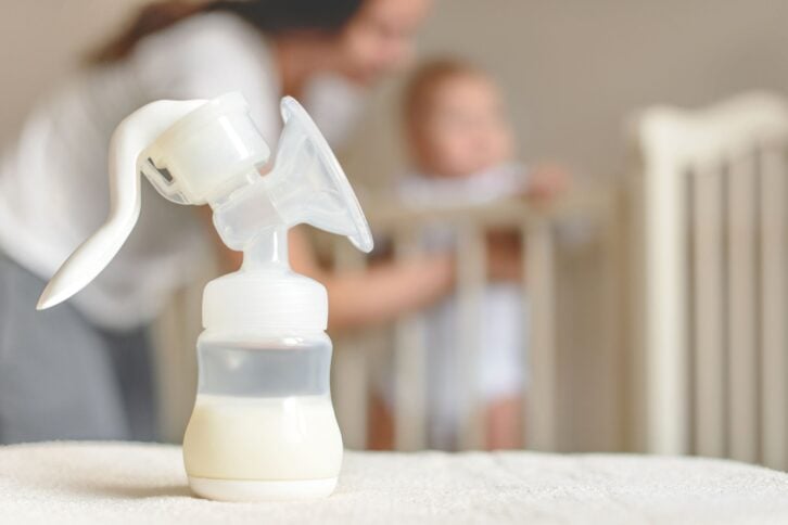 breast pump and bottle with breast milk on the background of mother and baby in bed