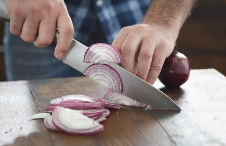 Close up male hands chopped fresh red onion on wooden table