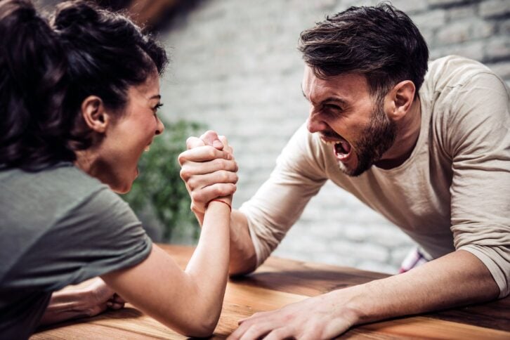 adult brother and sister shouting while arm wrestling at home