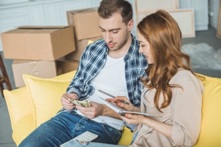young couple taking notes and counting money while moving home