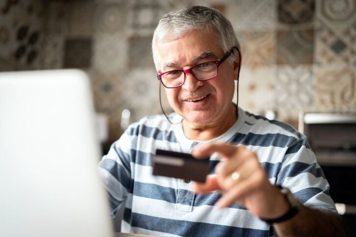 senior man holding credit card smiling with laptop open