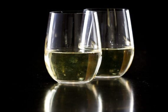two stemless white wine glasses on a black background