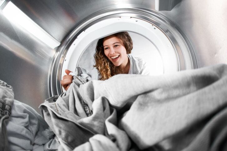 Distorted by fisheye lens a cute brunette woman loads or unloads a tumble dryer or washing machine;  the view is - unusually - from inside the drum.