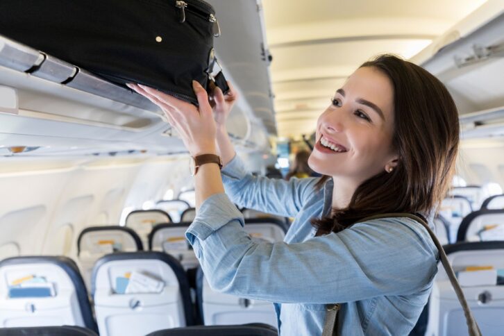 woman places luggage in airplane's overhead compartment