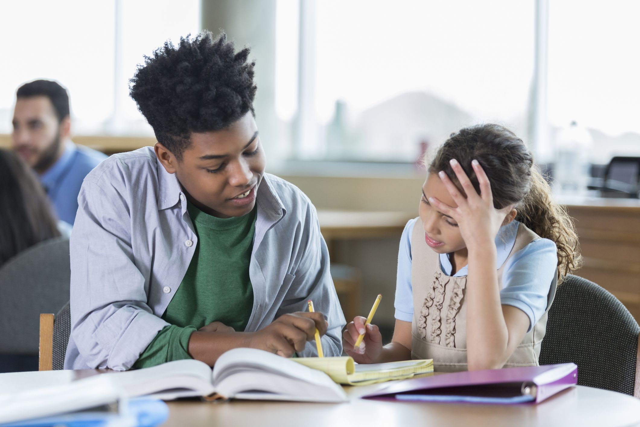 Male high school student helps an elementary school student with a math assignment. He is tutoring the elementary student after school.