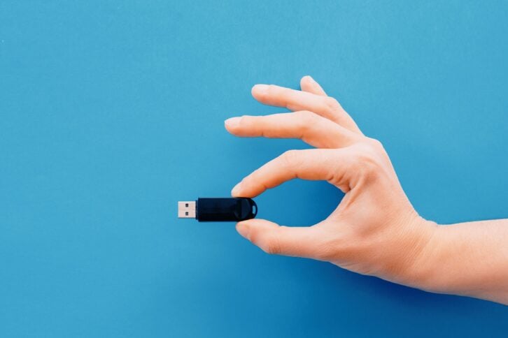 one hand holding a USB flash driver on blue background