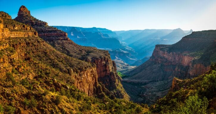 Panoramic vista down the Bright Angel Trail to the green oasis of Indian Garden and the early morning rays of sunlight illuminating the North Rim of the Grand Canyon National Park, Arizona, USA.