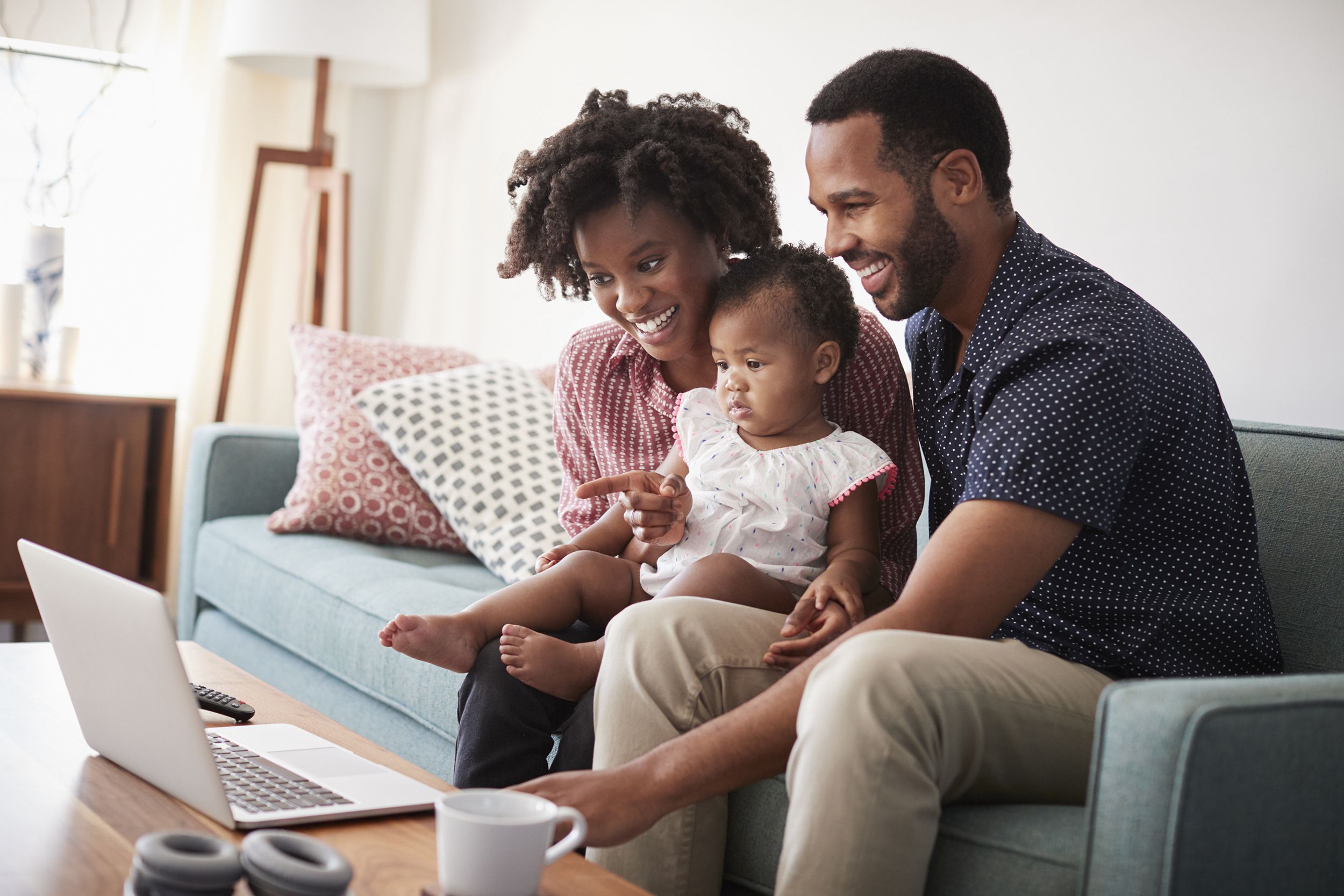family with baby daughter sitting on sofa at home looking at laptop