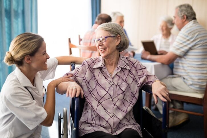nurse attending to a cheerful elderly woman sitting in a wheelchair in a nursing home