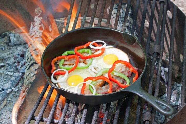 A breakfast of eggs on toast with bacon, onions and peppers frying on a grill