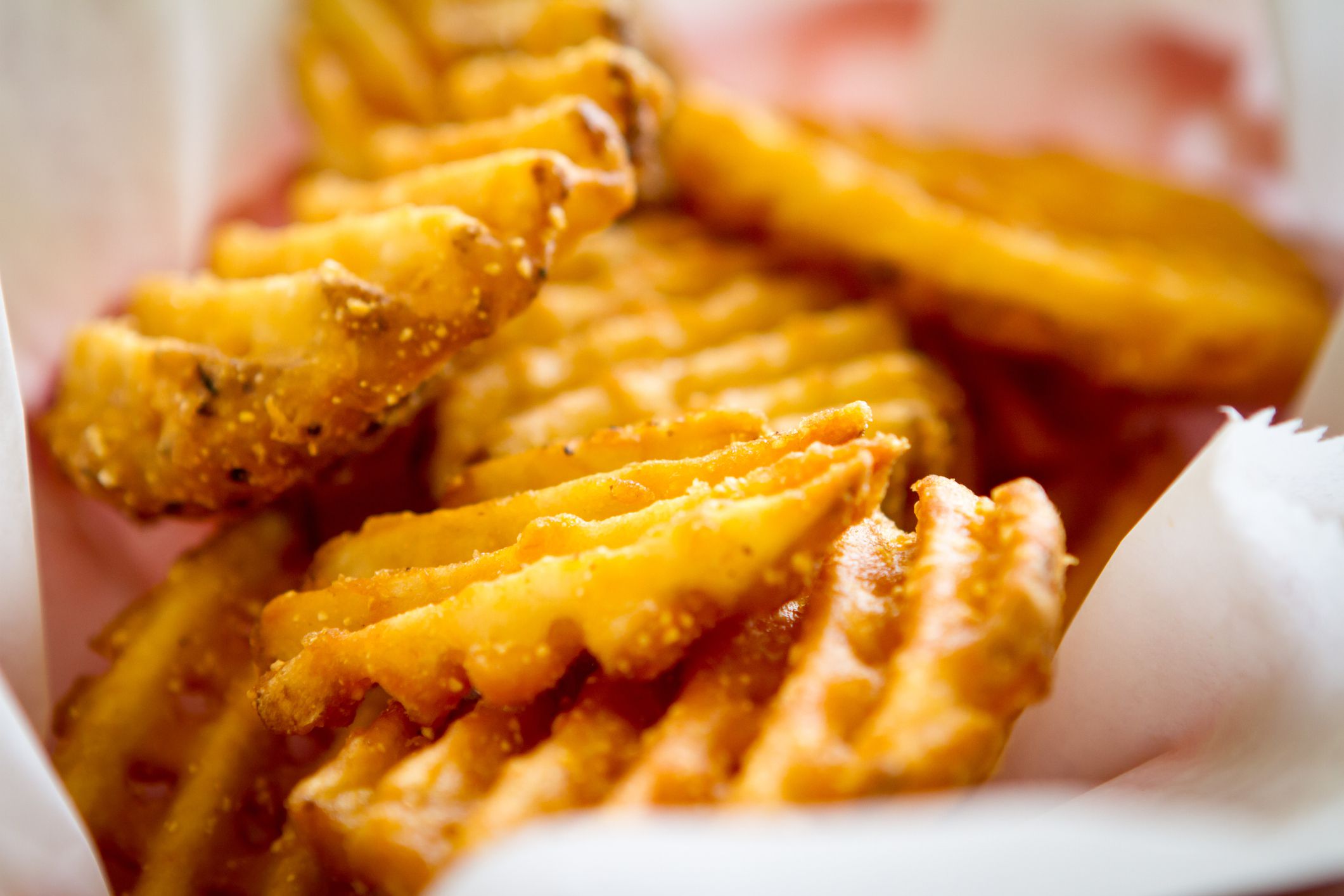 Close-up of golden, crispy waffle fries with ridged texture, served in a white paper-lined container.