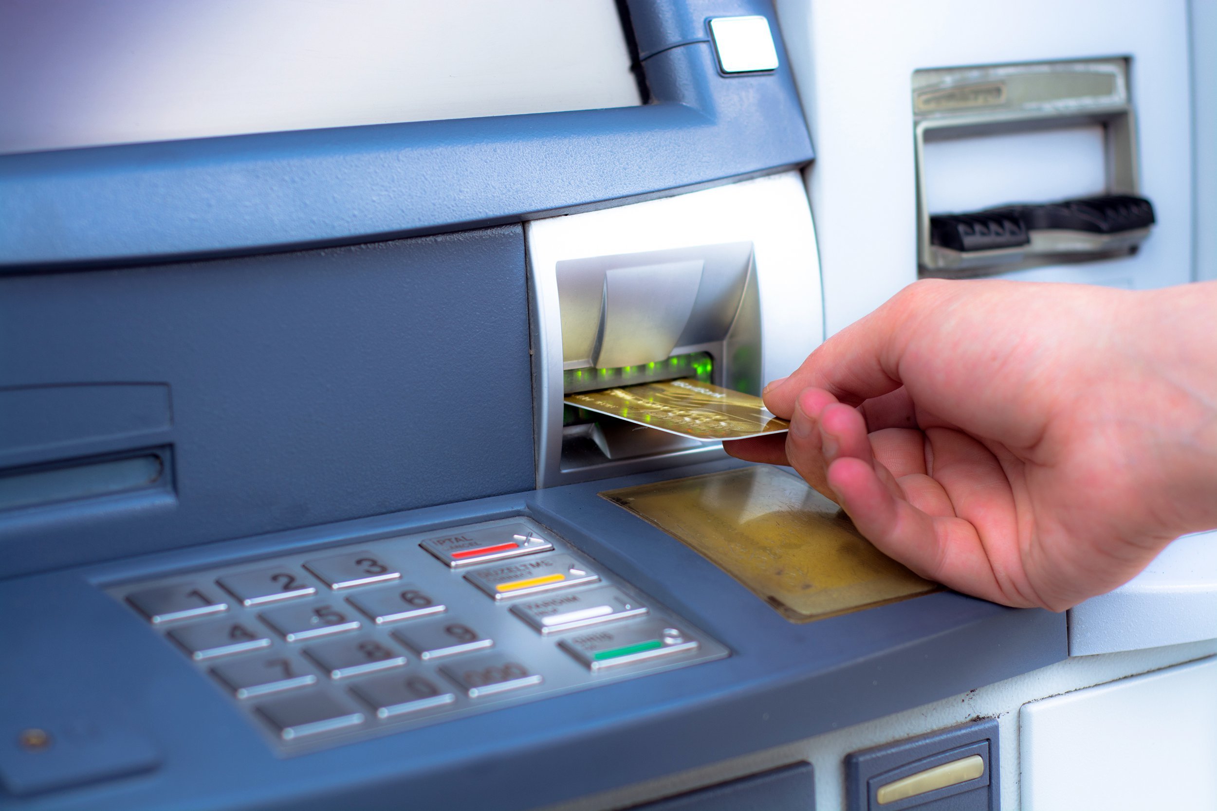 A person’s hand inserts a bank card into the card slot of an ATM machine, with the keypad and screen visible.