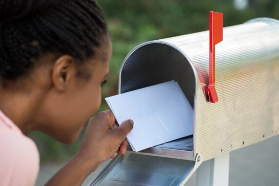 A woman placing a white envelope into a metal mailbox.