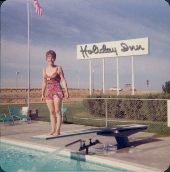 A woman in a floral swimsuit stands on a diving board in front of a Holiday Inn sign.