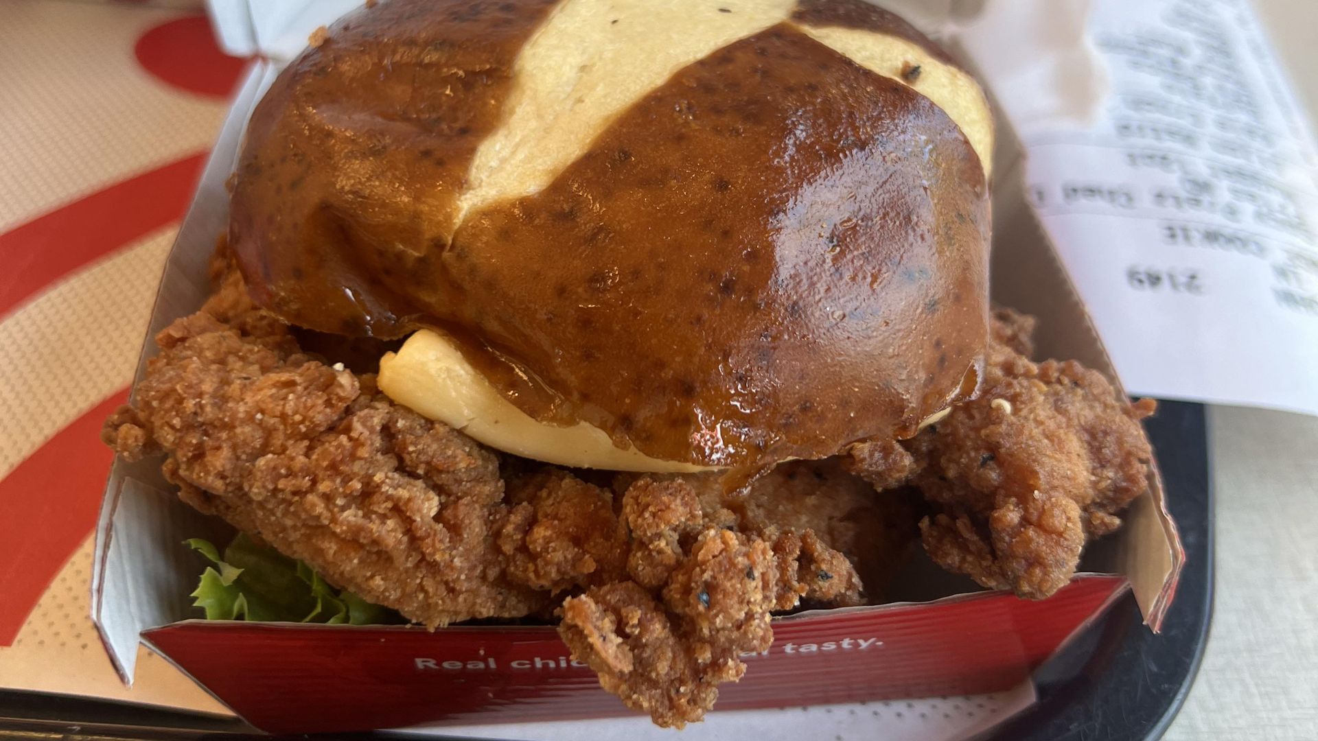 A Chick-fil-A crispy fried chicken sandwich with lettuce on a pretzel bun, served in a red box with a receipt and tray in the background—a must-try from the new fast-food menu.