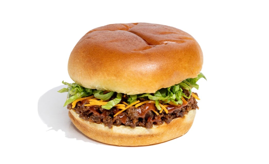 A new fast-food favorite, this sandwich features a soft, golden bun filled with shredded lettuce, grated cheddar cheese, and a loose, saucy ground beef mixture, shown on a white background.
