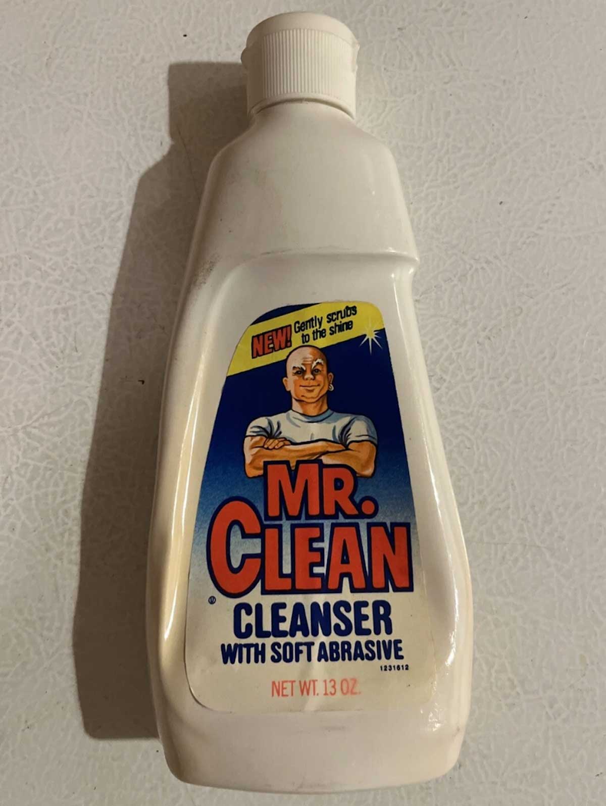 A bottle of Mr. Clean Cleanser with Soft Abrasive, featuring the iconic muscular, bald cartoon man in a white shirt—a true 1980s classic. The white bottle with a blue label holds 13 ounces.