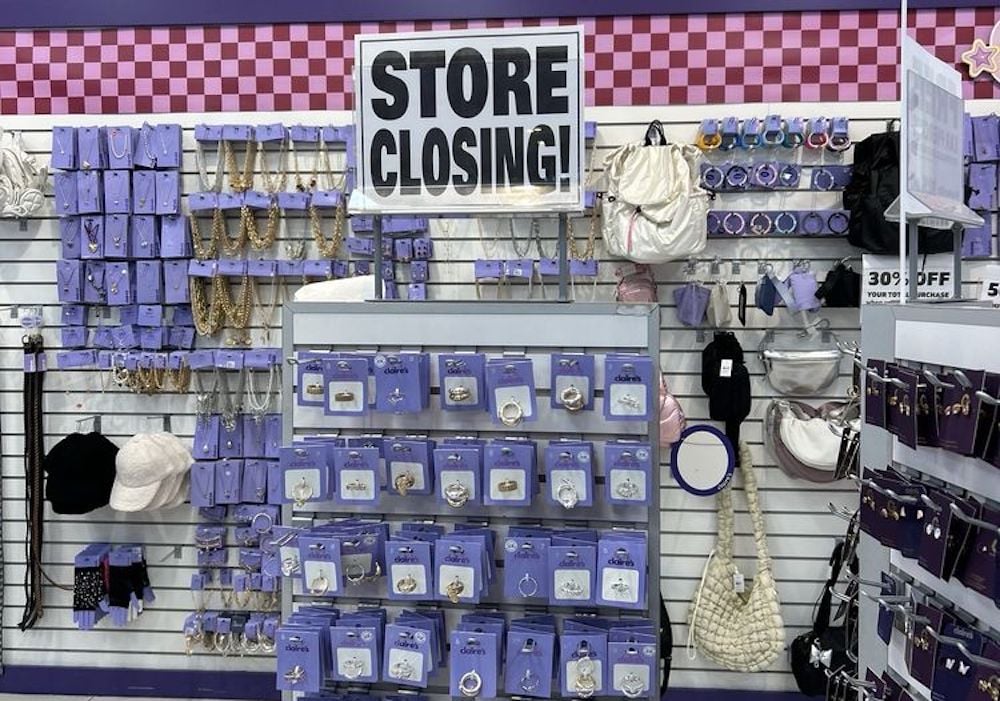 A retail display with jewelry, hats, and handbags, featuring a large "STORE CLOSING!" sign above. Many items are on hooks against a wall, with a discount sign and checkered purple trim along the top.