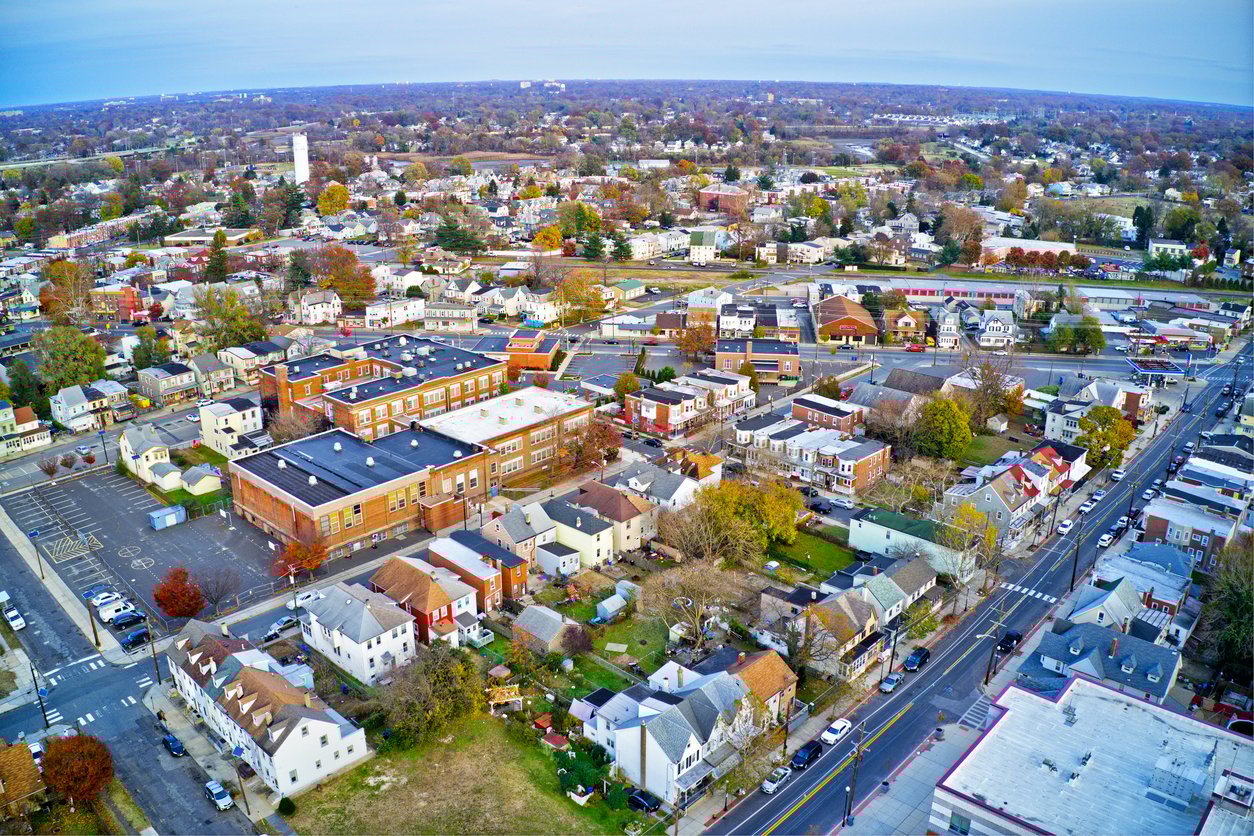 Aerial view of a suburban neighborhood with houses, a school building, trees with autumn foliage, and streets intersecting through the area under a cloudy sky.