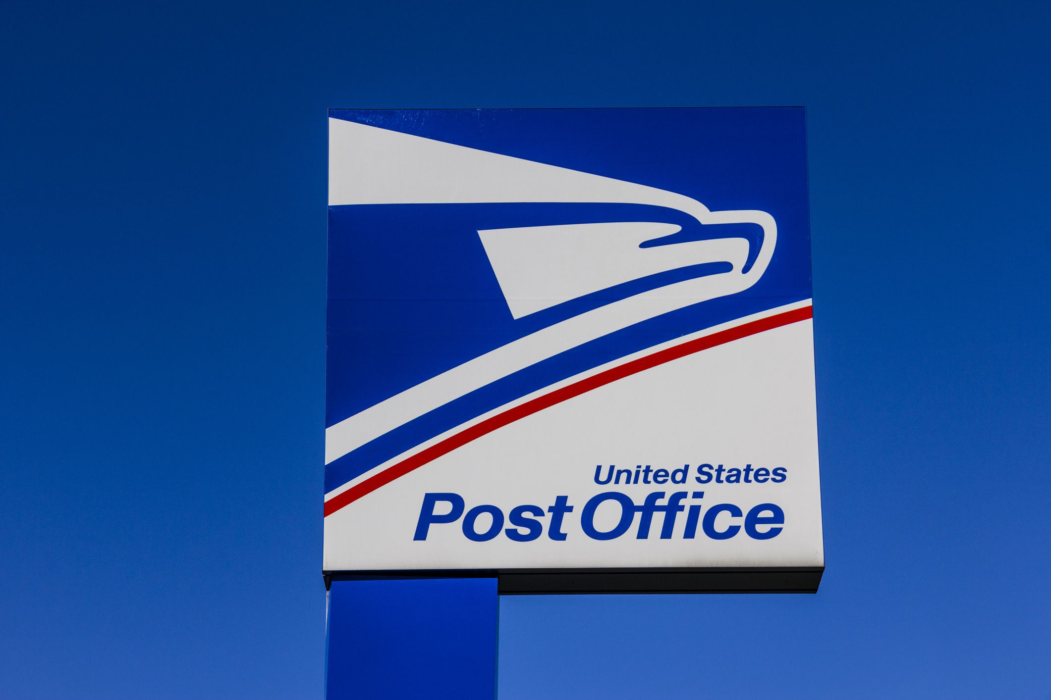 A large sign with the United States Postal Service eagle logo and the words "United States Post Office" set against a clear blue sky.